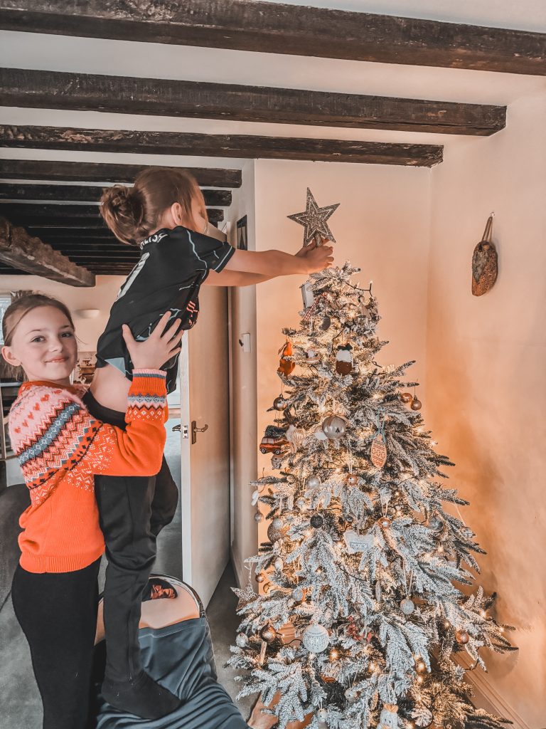 Older sister lifting younger brother to place star on top of Christmas tree
